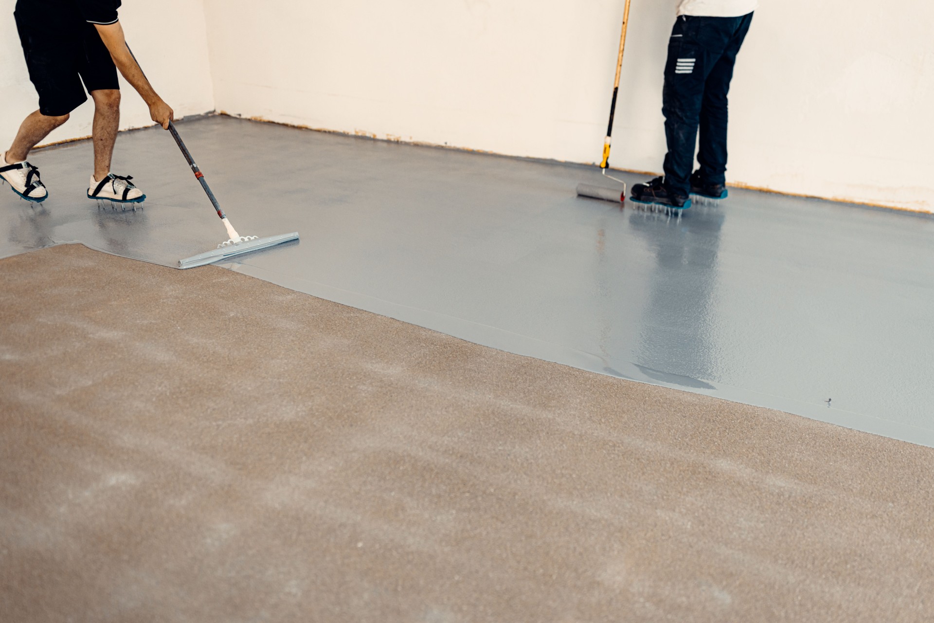 Construction workers applying grey epoxy resin in an industrial hall