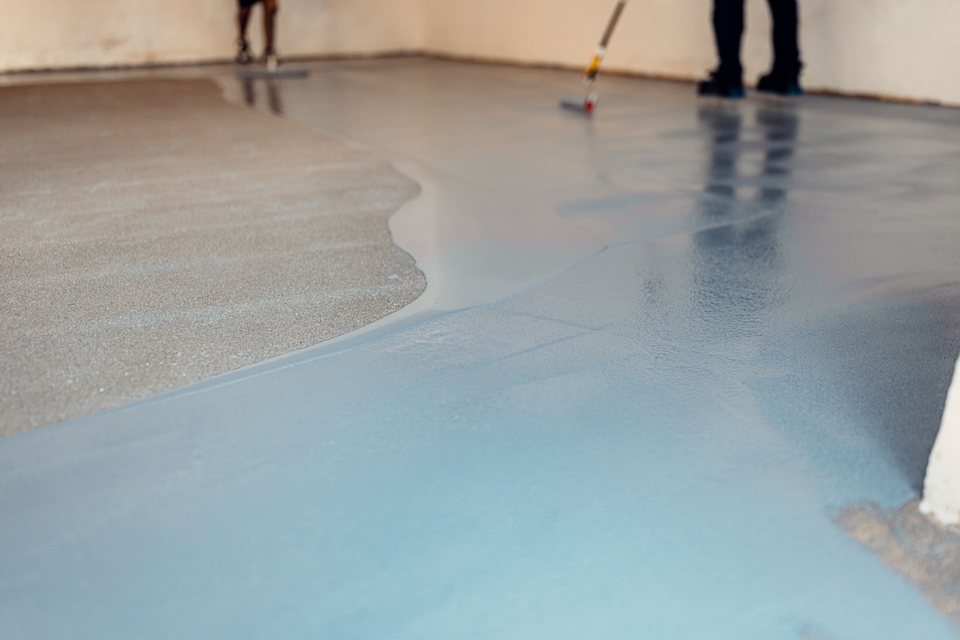 Construction worker apply grey epoxy resin in an industrial hall